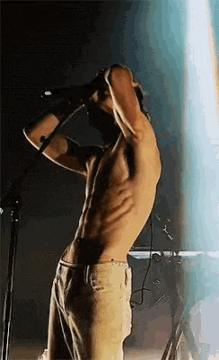 a shirtless man is singing into a microphone while standing on a stage .