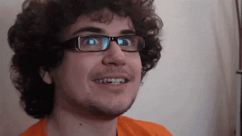 a man with curly hair wearing glasses is smiling