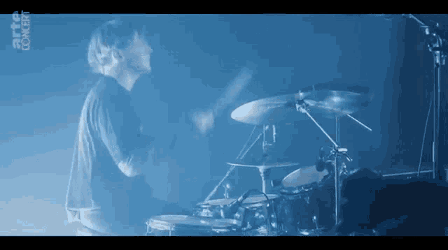 a man is playing drums in front of a blue background with the word concert written on it .