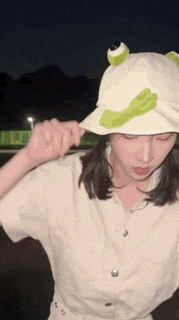 a woman wearing a white hat with a green frog on it .