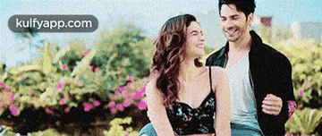 a man and a woman are sitting next to each other in a park and smiling .