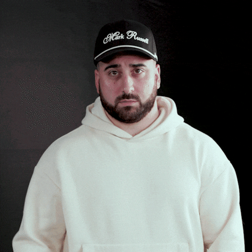 a man wearing a white hoodie and a black mark russell hat