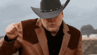a man wearing a cowboy hat and a brown jacket is pointing .