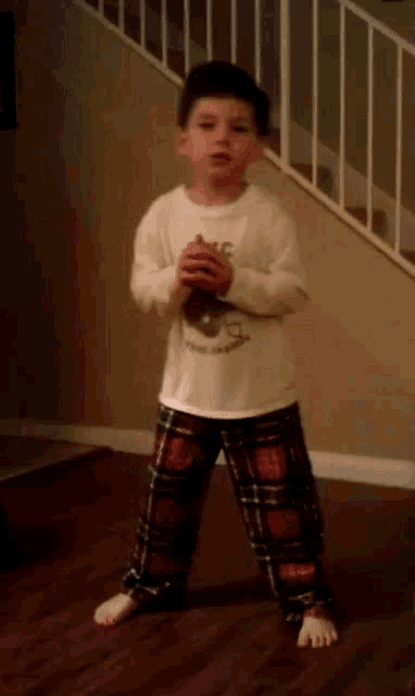 a young boy wearing plaid pants and a white shirt with a bear on it stands in front of stairs