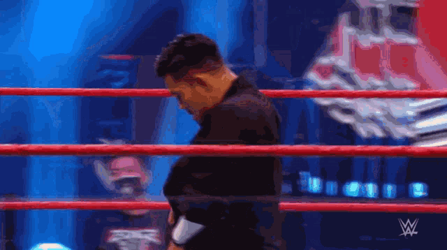 a man in a black suit is standing in a wrestling ring with a w logo in the background
