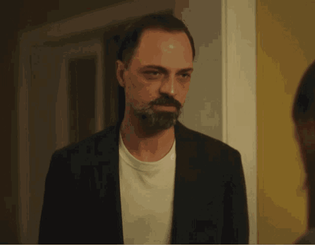 a man with a beard wearing a black jacket and a white shirt