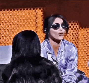 a woman wearing sunglasses and a purple shirt is sitting next to another woman .