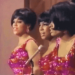 three women are standing next to each other in front of microphones on a stage .