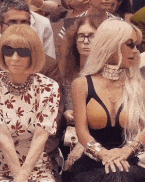 a woman wearing sunglasses sits next to another woman wearing a floral dress