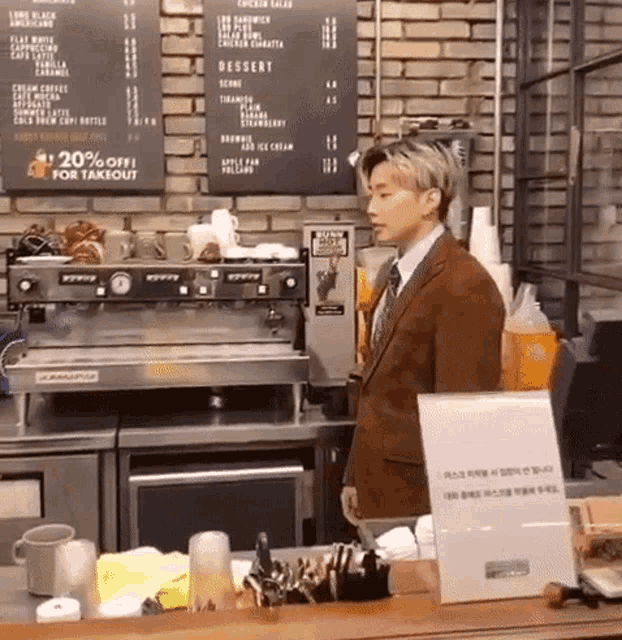a man in a suit and tie is standing behind a counter in a cafe .