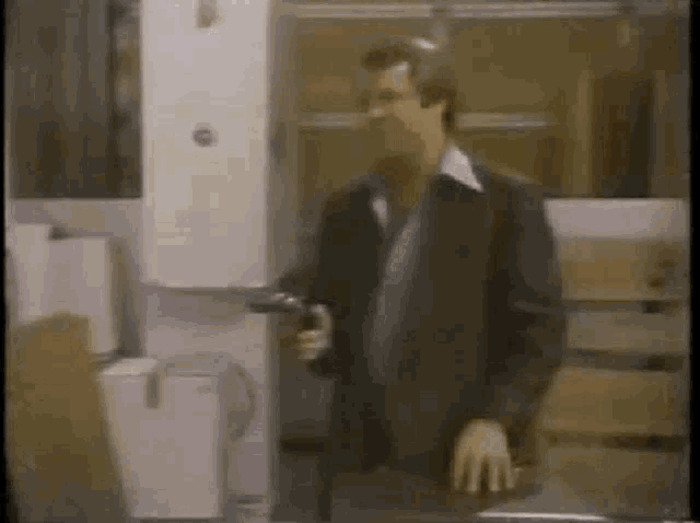 a man in a suit is holding a gun while standing in front of a water dispenser .