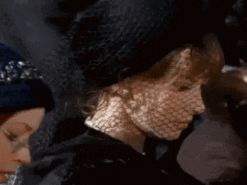a woman is wearing a black hat and veil .