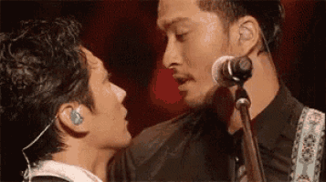 two men are kissing in front of a microphone while standing next to each other .