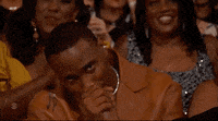 a man is sitting in a crowd of people with his hand to his mouth .