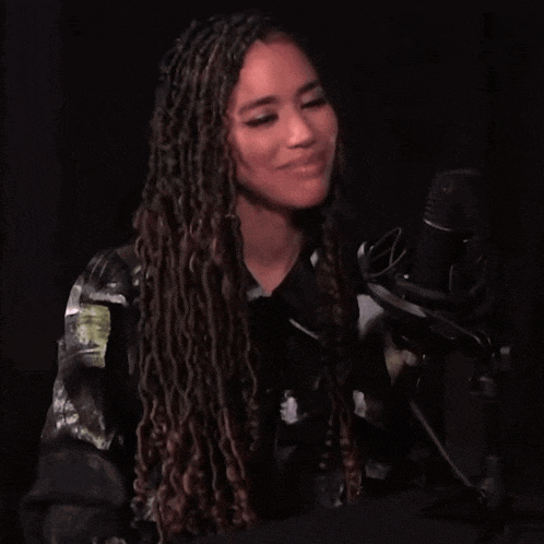 a woman with dreadlocks stands in front of a microphone and smiles
