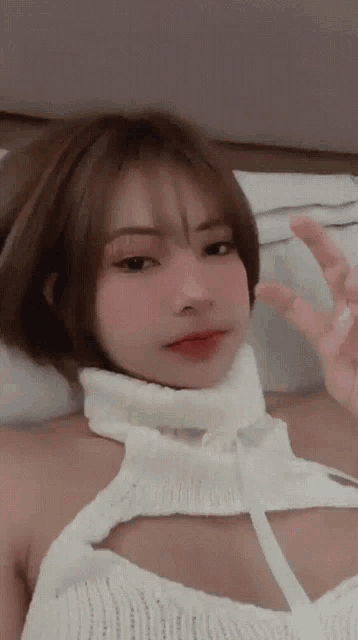 a woman in a white sweater is laying on a bed giving a peace sign