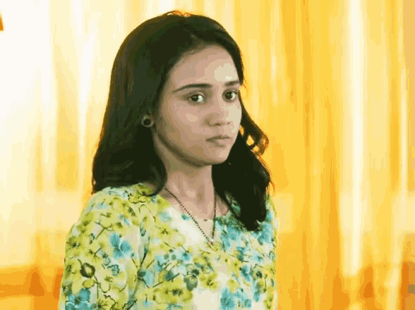 a young woman wearing a yellow and blue floral shirt is looking at the camera