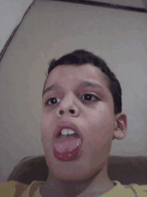 a young boy sticking his tongue out in a yellow shirt