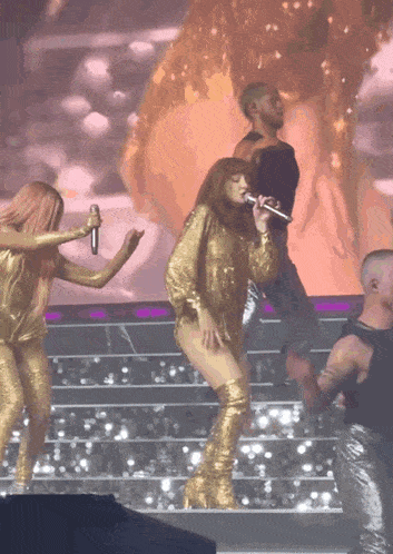 a woman in a gold outfit sings into a microphone on a stage