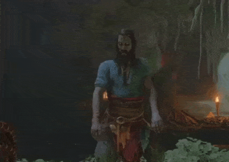 a man with long hair and a beard is dancing in a cave with his arms outstretched .