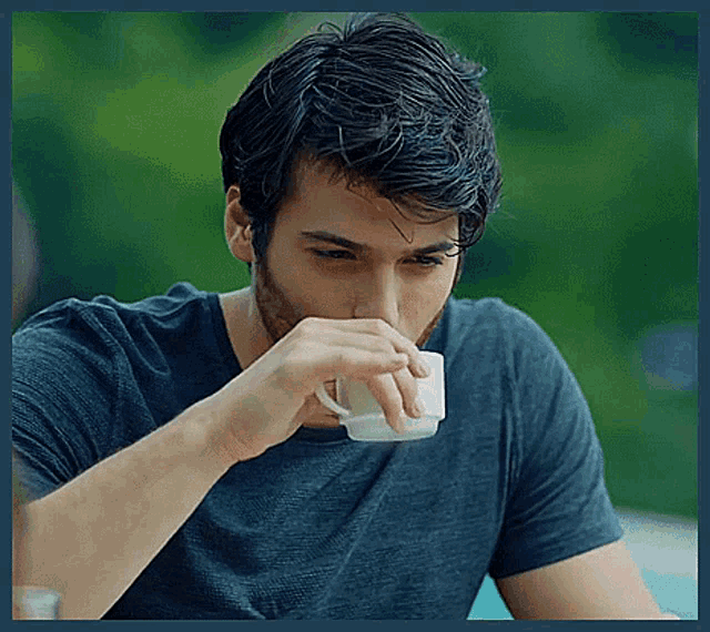 a man in a blue shirt is drinking from a cup