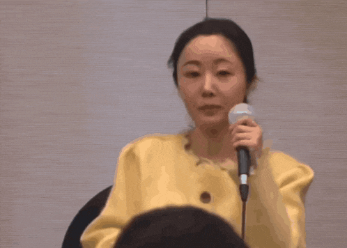 a woman in a yellow jacket is holding a microphone and speaking into it