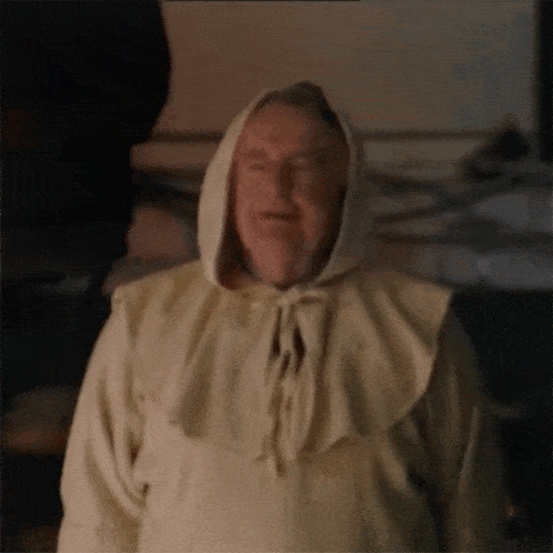 a man wearing a white robe with a hood on his head is standing in a dark room .