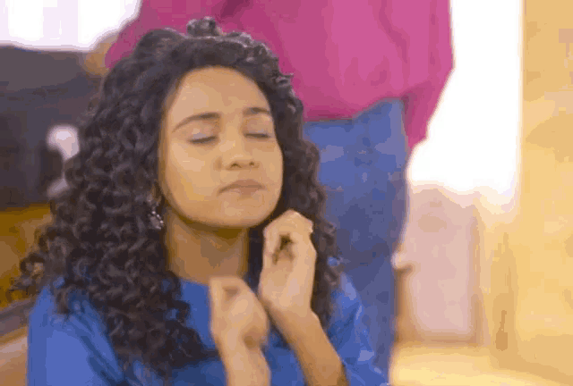 a woman with curly hair is wearing a blue shirt and has her eyes closed