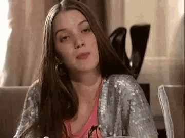 a woman with long hair is sitting at a table with a cup of coffee and looking at the camera .