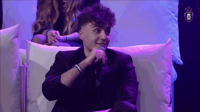 a man sitting on a couch holding a microphone and wearing a wristband that says ' jesus '