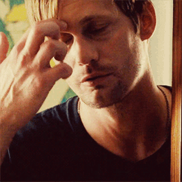 a man in a black shirt is touching his face