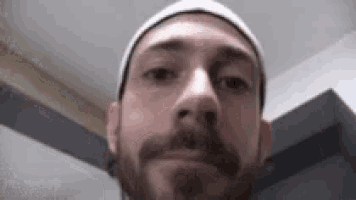a man with a beard and a beanie is looking at the camera .