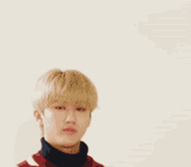 a young man with blonde hair is wearing a red and black sweater and a black turtleneck .