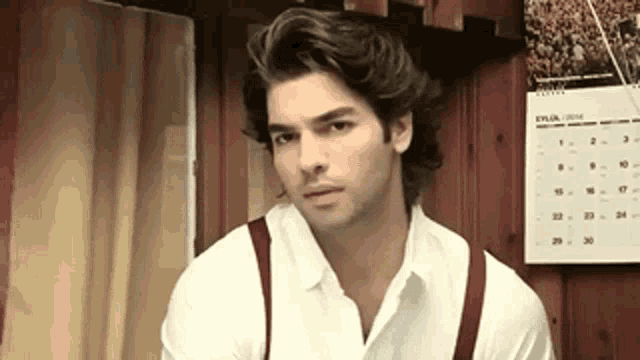 a man wearing suspenders and a white shirt is standing in front of a calendar that says eylia