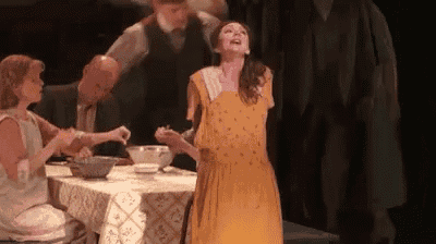 a woman in a yellow dress is standing in front of a table with a bowl of food on it .