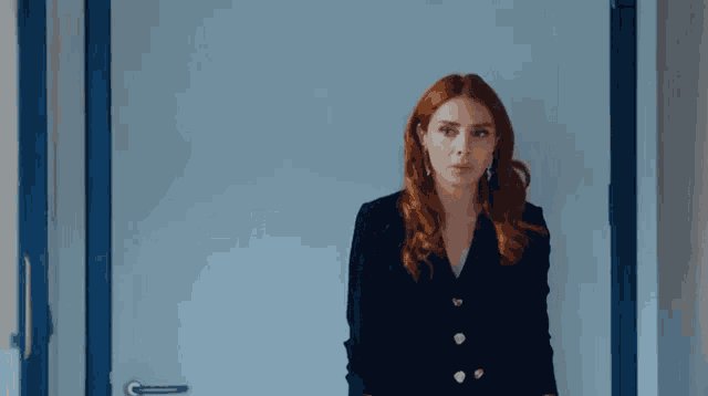 a woman with red hair is standing in front of a blue door and looking at the camera .