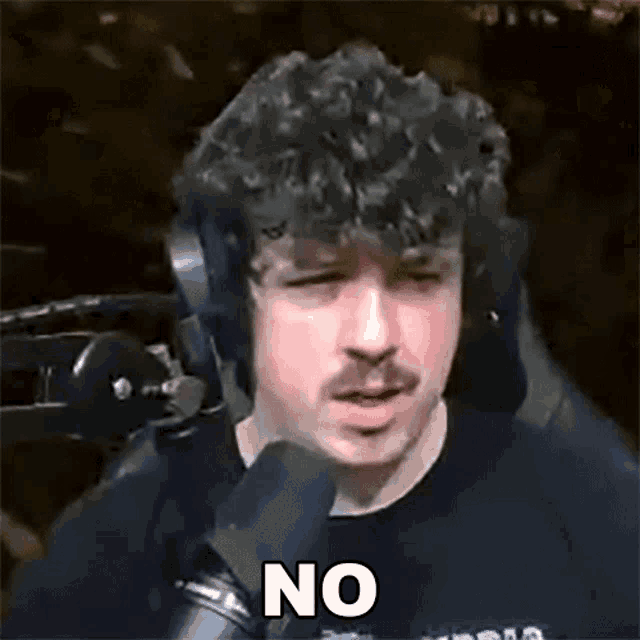 a man with curly hair and a mustache is sitting in front of a microphone and making a funny face .
