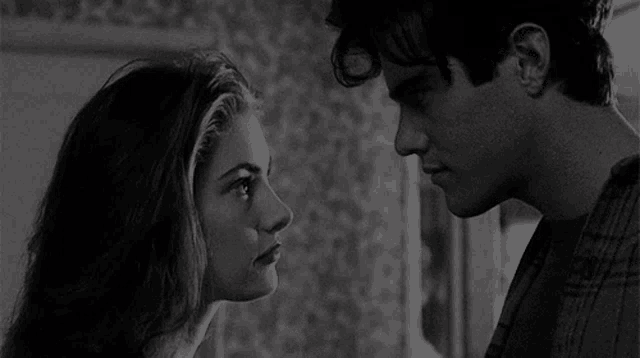 a black and white photo of a man and a woman looking into each other 's eyes .