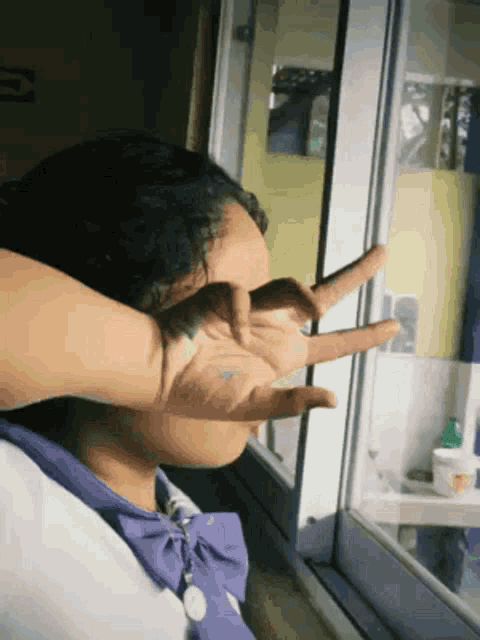 a woman covering her face with her hands while looking out of a window