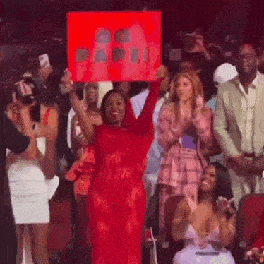 a woman in a red dress is holding a sign in front of a crowd of people at a concert .