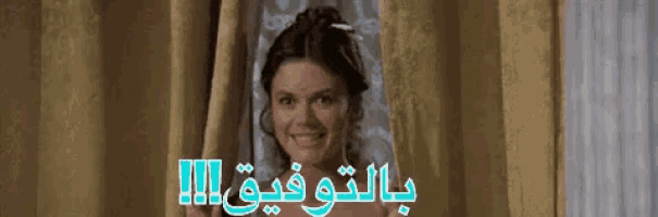 a woman is smiling while peeking out of a window with arabic writing on it .