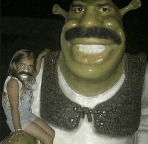 a little girl is sitting next to a shrek statue with a fake mustache .