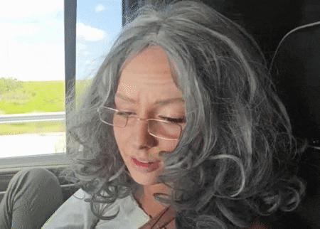 a woman wearing a gray wig and glasses looks down
