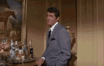 a man in a suit and tie is standing in front of a table with bottles of alcohol on it
