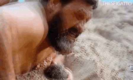 a man with a beard is laying in the sand on the beach with his head in the sand .