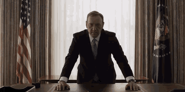 a man in a suit and tie is sitting at a desk with his hands on the table .