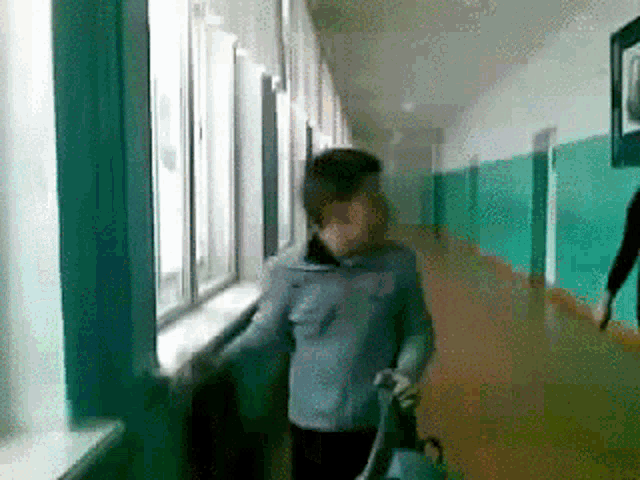 a man in a blue jacket is walking down a hallway looking out a window