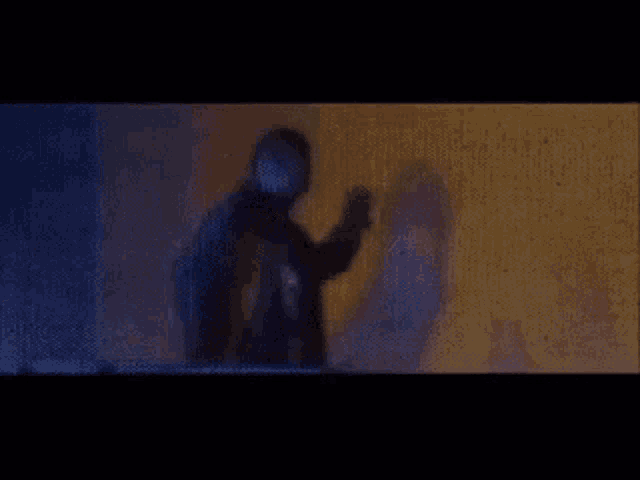 a man in a mask is standing in front of a wall with his shadow on the wall .