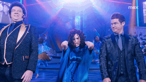a man in a suit stands next to a woman in a blue dress and a man in a black suit and tie