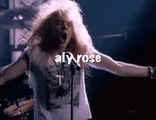 a man with long blonde hair is singing into a microphone on stage .